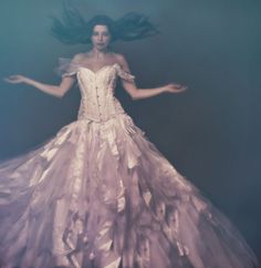 a woman in a white dress with her arms out and hair flying through the air