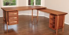 a wooden desk sitting on top of a hard wood floor next to two large windows