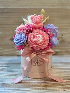 a pink and purple flower arrangement in a small metal container on a wooden table with ribbon