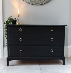 a black dresser with gold handles in front of a wall clock and potted plant