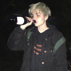 a young man drinking from a bottle while standing in front of a forest at night