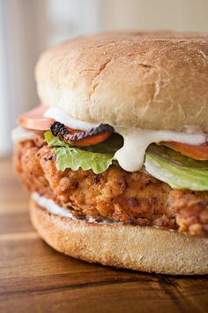 a chicken sandwich with lettuce, tomato and cheese on a wooden table top