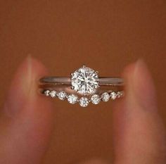 a woman's hand holding a diamond ring on top of her finger, with the engagement band set in white gold