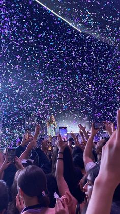 a crowd of people at a concert with confetti falling from the ceiling and on their cell phones