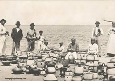 an old black and white photo of people standing near the ocean with pots on the beach