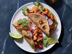 two tacos on a plate with limes and cilantro next to it