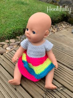 a small doll sitting on top of a wooden table next to grass and rocks in the background