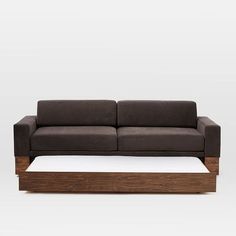 a brown couch sitting on top of a wooden table next to a white wall and floor