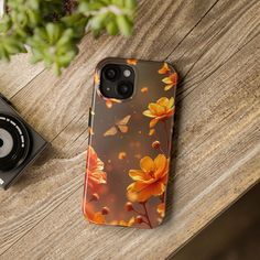 an iphone case with orange flowers on it sitting next to a camera and a plant