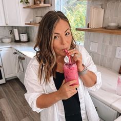 a woman drinking a pink smoothie in her kitchen