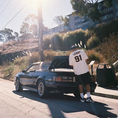 a man standing next to his car on the side of the road in front of some buildings