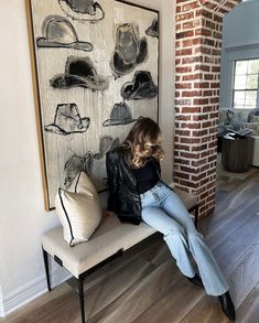 a woman sitting on a bench in front of a wall with hats hanging on it