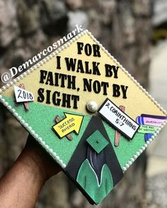 a hand holding a decorated graduation cap that says for i walk by faith, not by sight