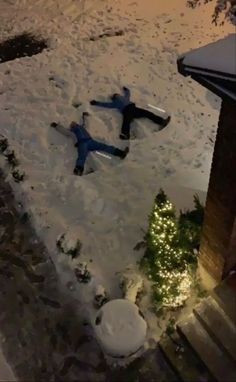 two people laying in the snow next to a christmas tree