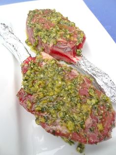 two steaks covered in pesto on top of a white plate with a fork