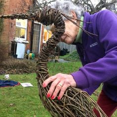 an older woman is making a wicker wreath out of branches in the yard with her hands