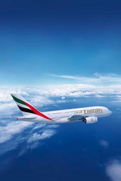 an emirates airplane flying above the clouds in the blue sky with white and red stripes