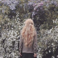 a woman with long blonde hair is standing in front of some white and purple flowers