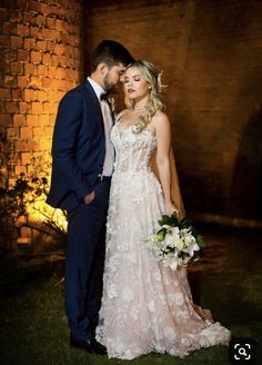 a bride and groom pose for a photo in front of a brick wall at night