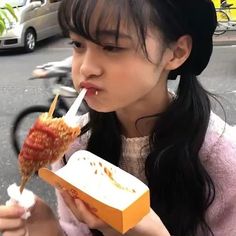 a woman eating food from a box on the street