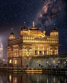 the golden building is lit up at night with stars in the sky above it and water below