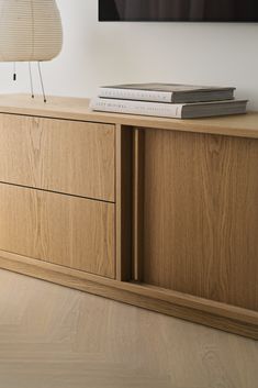 a wooden cabinet with two books on top and a lamp next to it in front of a flat screen tv