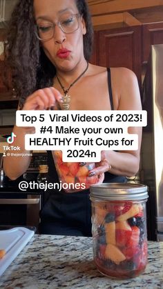 a woman holding a jar filled with fruit on top of a counter