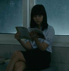 a woman sitting on a window sill reading a book