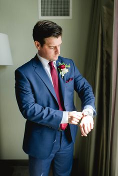 a man in a blue suit and red tie is looking down at his wrist watch