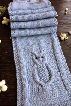 four knitted towels are stacked on top of each other, with an owl motif