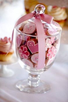 a glass filled with lots of pink and white heart shaped cookies on top of a table