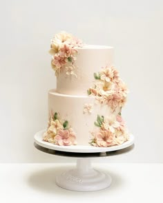 a three tiered wedding cake with flowers on the top and bottom, sitting on a white pedestal