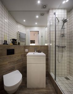 a white toilet sitting next to a bathroom sink under a shower stall with tiled walls