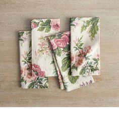 four napkins with pink flowers on them sitting on top of a wooden table next to each other