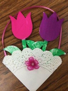 some paper flowers are sitting on top of a piece of white doily with pink and green leaves