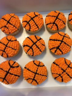 cupcakes decorated with orange frosting and black basketball balls are on a white tray