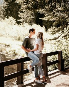 a man and woman standing next to each other on a wooden bridge near a river