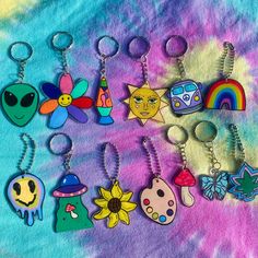 several different key chains are on a tie dye background, one has an alien face and the other has a rainbow