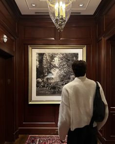 a woman standing in front of a painting on the wall next to a chandelier