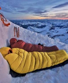 a man sleeping on the side of a snow covered mountain at night with his arms wrapped in a sleeping bag