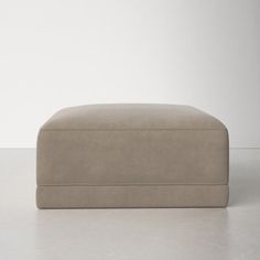 a beige footstool sitting on top of a white floor next to a wall