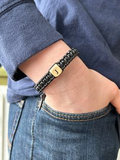 a person wearing a black bracelet with a gold clasp on their left wrist and the letter i on it