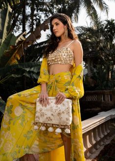 Editor's Note Featuring a yellow gathered dhoti skirt and romantic long jacket with poetic sleeve details. The blouse features dainty ivory and yellow floral print with kaudi shells and coin detailing and it has been hand tucked. Color: Yellow Fabric: Crepe, cotton silk Component: Jacket, skirt and blouse Fit: Fitted at bust and waist, blouse: back opening, dhoti skirt: side zip attached lining: blouse and skirt Occasion: Resort and party Care: Dry Clean Only About the Designer Paulmi & Harsh is Yellow Bohemian Saree Set, Bohemian Yellow Saree Set, Yellow Bohemian Saree Dress, Yellow Bohemian Festive Sets, Bohemian Festive Yellow Set, Dhoti Skirt, Jacket And Skirt Set, Blouse Yoke, 1950’s Fashion