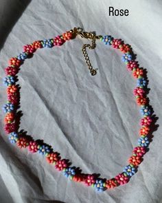 a multicolored beaded necklace is displayed on a piece of white paper with the words rose written in gold