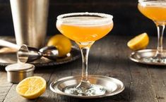 two cocktail glasses filled with orange juice and topped with sugar sit on a wooden table