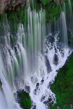 the water is flowing over the rocks and green mossy plants on the side of the waterfall