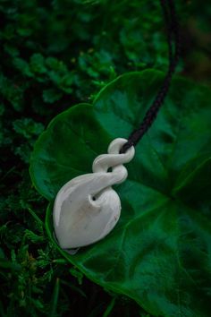 a white necklace on a green leaf in the grass with black cord hanging from it's end