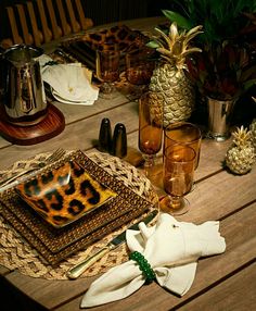 a table topped with plates and napkins next to pineapples on top of a wooden table