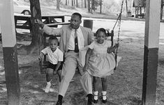 a man sitting on a swing with two children