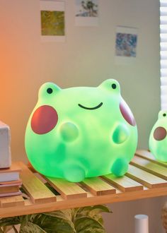 a green frog lamp sitting on top of a wooden shelf next to a potted plant